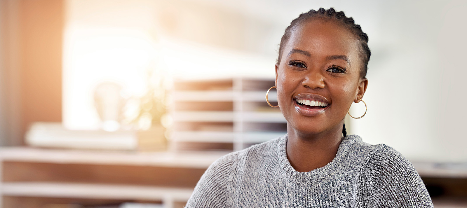 A woman with a radiant smile is seated in front of a blurred background, possibly an office setting.