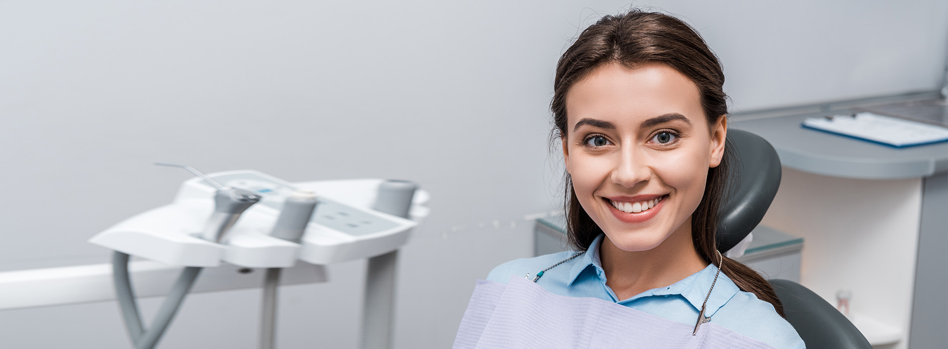 A woman in a dental office, smiling and wearing a blue shirt.