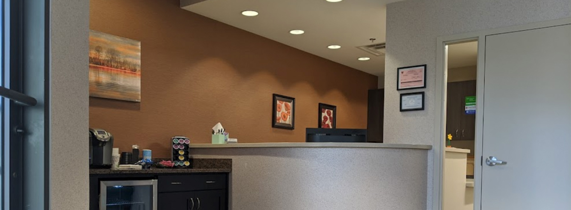 The image depicts a well-lit office interior with a reception desk and counter, featuring a modern design with neutral tones and a clean appearance.